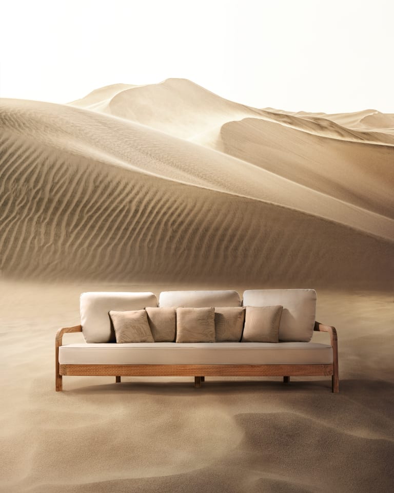 Photograph of a sofa placed on the sand in a desert with dunes in the background