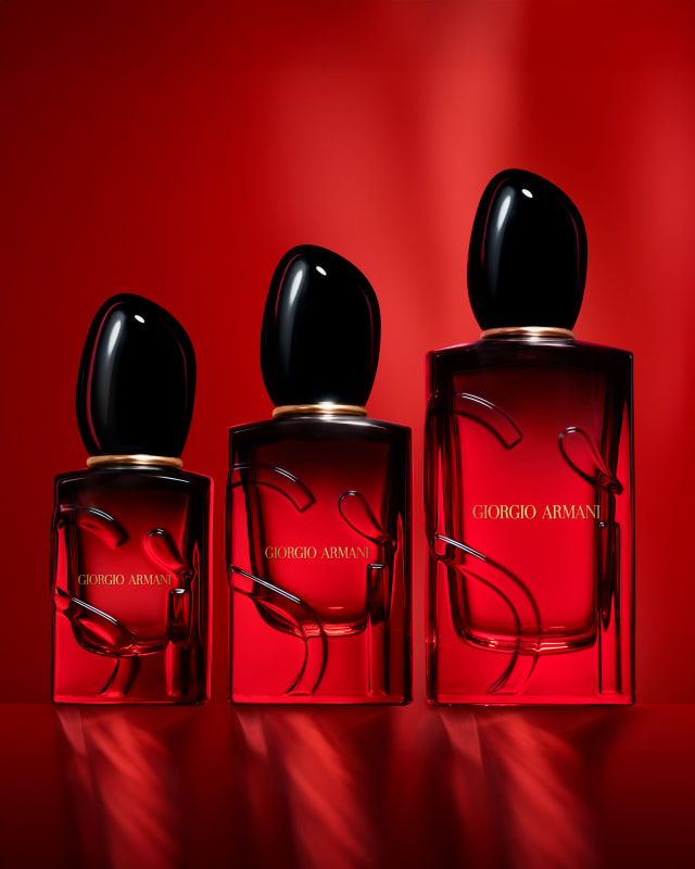 Fotografie di tre boccette di profumo Sì Giorgio Armani in tre diversi formati posizionate su sfondo rosso